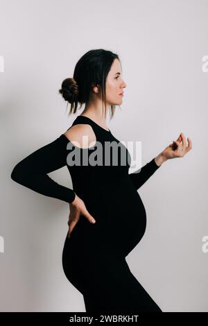 Elegante Erwartung: Ein Profil von Stärke und Gnade. Schwangere Frau im schwarzen engen Kleid. Wunderschöne Silhouette Stockfoto