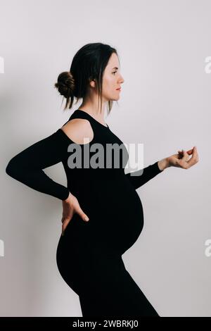 Elegante Erwartung: Ein Profil von Stärke und Gnade. Schwangere Frau im schwarzen engen Kleid. Wunderschöne Silhouette Stockfoto