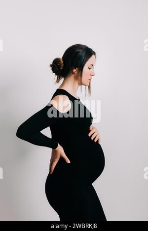 Elegante Erwartung: Ein Profil von Stärke und Gnade. Schwangere Frau im schwarzen engen Kleid. Wunderschöne Silhouette Stockfoto