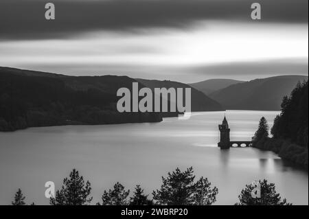 Langlebigkeit, schwarz-weiß, des Lake Vyrnwy in Mid Wales. Es gibt eine Pumpstation, die in den See ragt, der von üppigem Grün umgeben ist Stockfoto