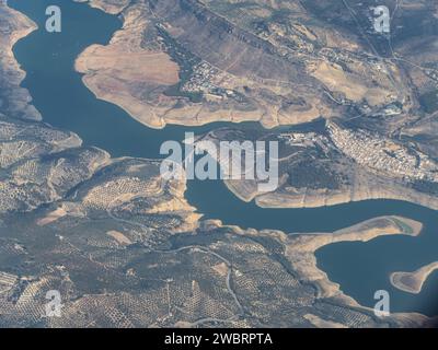 Aus der Vogelperspektive auf den Wasserspeicher in Iznajar, Andalusien, Spanien, mit der Puente Agroman Brücke, Wasserdamm, Dorf, geschwungenem Fluss, sanften Hügeln, oli Stockfoto
