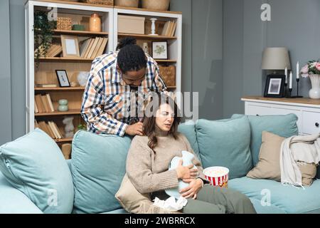 Gemischte Rasse Paar afroamerikanischer Mann und weiße Frau, männlich massieren seine Freundin oder Frau in ihrer Menstruation, während sie zu Hause sitzen. Liebe, Suppo Stockfoto