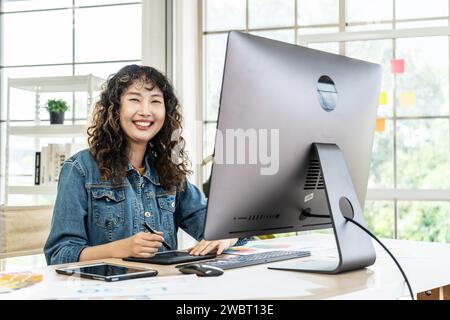 Eine junge asiatische Grafikdesignerin, die in einem Büro mit einem Computer arbeitet Stockfoto