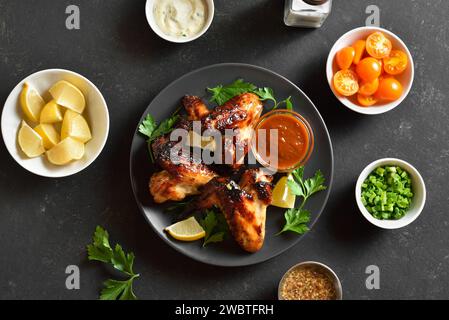 BBQ Hähnchenflügel auf Teller über schwarzem Steinhintergrund. Leckeres gegrilltes Hähnchenfleisch zum Abendessen. Draufsicht, flach Stockfoto