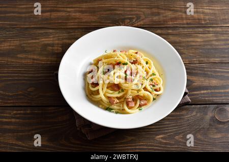 Carbonara-Pasta, Spaghetti mit knusprigem Pancetta-Speck und schwarzem Pfeffer auf weißem Teller auf Holztisch. Traditionelle italienische Küche. Landhausstil, Close Stockfoto
