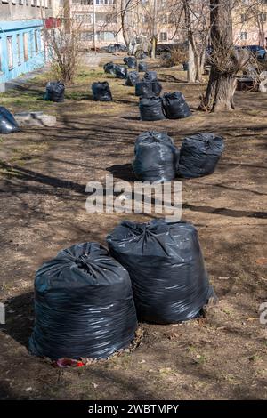 Schwarze Säcke mit Müll im Park, alte umgestürzte Blätter, Äste auf dem Boden. Ein Haufen Taschen. Frühjahrsputz. Stadtreinigung. Stockfoto