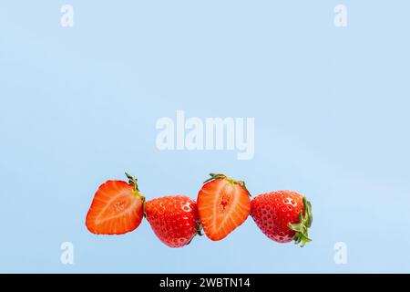 In Stücke geschnitten und ganze Erdbeeren hintereinander auf blauem Hintergrund, eine Kopie des Raumes. Leckeres und gesundes Essen. Natürliche Vitamine. Sommerdiät f Stockfoto