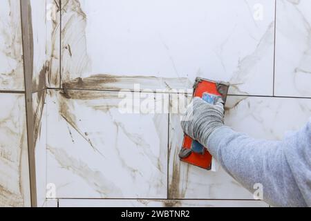 Fliesen füllen Lücken zwischen Keramikfliesen mit Gummikelle beim Verfugen von Keramikfliesen. Stockfoto