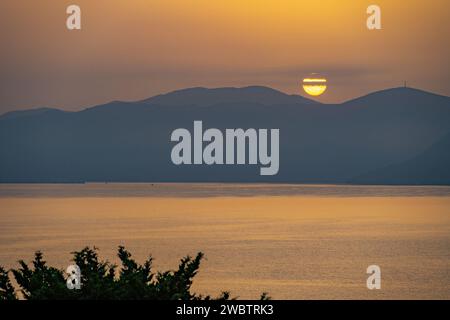 Sonnenaufgang hinter den Bergen des griechischen Festlandes von der Insel Meganisi im Ionischen Meer Stockfoto