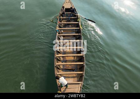 Blick von oben auf ein Holzboot, das auf grünem Wasser rudert, von einer Gruppe von Kindern in Indien Stockfoto