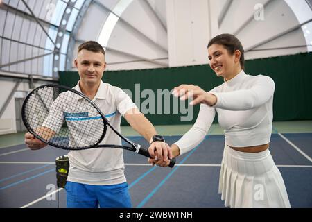 Junger Mann, der der Frau beibringt, wie man Tennisschläger fängt Stockfoto