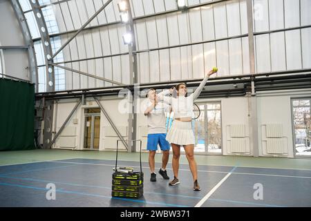 Der männliche Ausbilder konzentriert sich darauf, Tennisspielerinnen die Technik des Servierens zu vermitteln Stockfoto