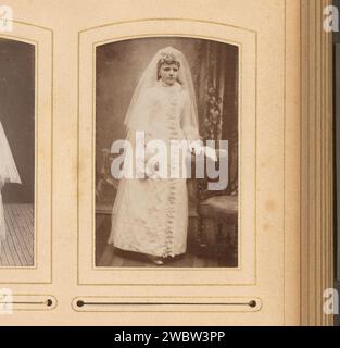 Porträt eines Mädchens im Kommunionkleid, stehend an einem Stuhl, Hermanus Jodocus Weesing, 1868 - 1900 Foto. Visitenkarte dieses Foto ist Teil eines Albums. Unterstützung für Fotos in Amsterdam. Pappalbumendruck historische Personen - BB - Frau. Mädchen (Kind zwischen Kleinkind und Jugend). Kommunionkleid. Stuhl Stockfoto