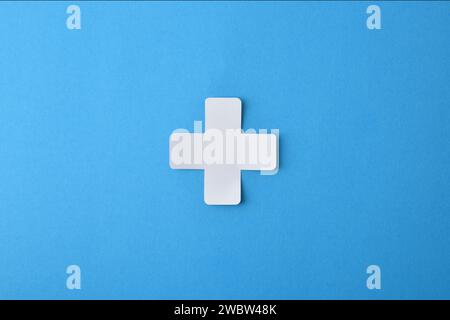 Konzeptuelle Medizin-Symbol mit kreuzförmigem Papierausschnitt isoliert in der Mitte auf blauem Hintergrund. Stockfoto