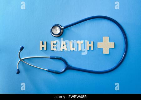Gesundheitshintergrund mit Stethoskop und Gesundheitsbotschaft mit Holzbuchstaben auf blauem Hintergrund. Draufsicht Stockfoto