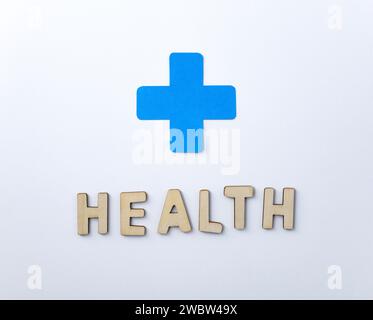 Hintergrund mit Ausschnitten von Holzbuchstaben, die das Wort Gesundheit und blauer Gesundheit Kreuzausschnitt auf weißem Hintergrund bilden. Draufsicht Stockfoto