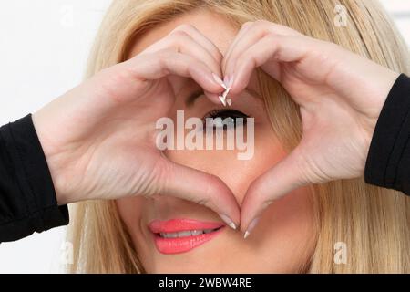 Frau, die eine Herzform mit den Händen vor ihrem Gesicht macht Stockfoto