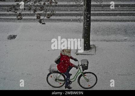 Winter-Eleganz: Ein rotbeschichteter Radfahrer fährt durch die verschneiten Straßen einer ostdeutschen Stadt im Bundesland Brandenburg Stockfoto