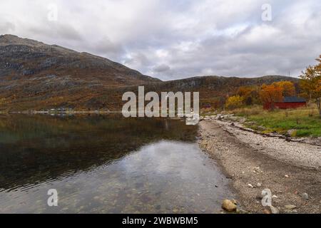 Panorama mit Schiff auf dem Fjord, zwischen steilen Bergen, Dorf am Ufer des Nordatlantiks. Bootshaus und hölzernes Ferienhaus Stockfoto