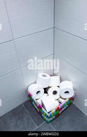 Ein Haufen Toilettenrollen in einem bunten Korb in der Ecke einer Toilette oder eines Wasserschranks Stockfoto