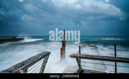 Ein hölzerner Pier, umgeben von der Kraft hoher Wellen und stürzenden Wellen, schafft eine dramatische und fesselnde Szene Stockfoto