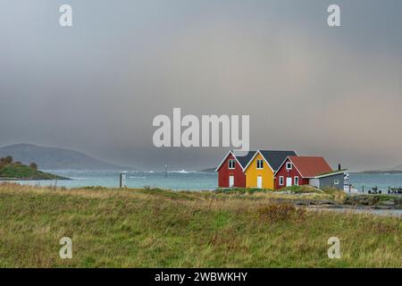 rote und gelbe Häuser am Strand des Atlantik auf der Insel Hillesøya bei Sommarøy, Troms, Norwegen. Landschaft Kalenderfoto mit Bergen im Hintergrund Stockfoto