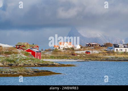 rote und gelbe Häuser am Strand des Atlantik auf der Insel Hillesøya bei Sommarøy, Troms, Norwegen. Landschaft Kalenderfoto mit Bergen im Hintergrund Stockfoto