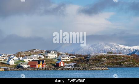 rote und gelbe Häuser am Strand des Atlantik auf der Insel Hillesøya bei Sommarøy, Troms, Norwegen. Landschaft Kalenderfoto mit Bergen im Hintergrund Stockfoto