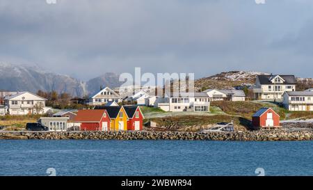 rote und gelbe Häuser am Strand des Atlantik auf der Insel Hillesøya bei Sommarøy, Troms, Norwegen. Landschaft Kalenderfoto mit Bergen im Hintergrund Stockfoto