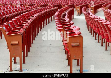 Flacher Blick über endlose gekrümmte Reihen roter Kunststoffsitze in einem Stadion oder einer Arena, das ansonsten völlig leer ist Stockfoto