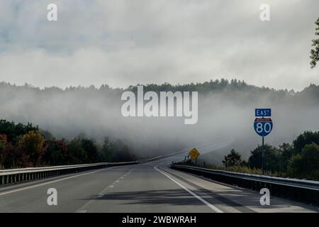 Fahrerperspektive auf der Autobahn I-80 in der Nähe von Clearfield, PA, USA, mit Sonnenschein auf niedrigem Nebel zwischen Bäumen und hügeliger Landschaft Stockfoto