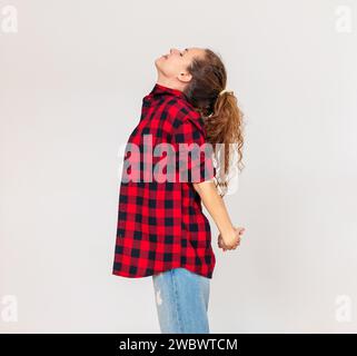 Brünette Frau in rotem Hemd steht vor einem einfachen, schlichten Hintergrund und dehnt ihren Körper aus. Stockfoto