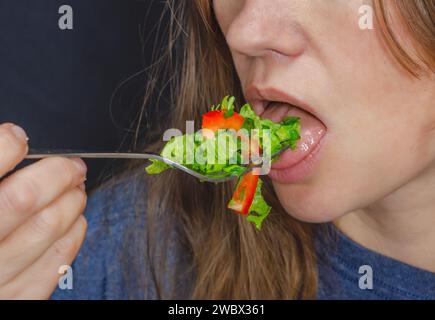 Salat auf Gabel im Mund einer Frau. Ein Teil des Gesichts einer Frau, die einen Salat isst. Gesunde Ernährung. Stockfoto