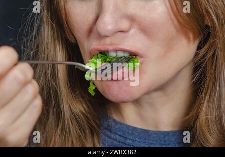 Salat auf Gabel im Mund einer Frau. Ein Teil des Gesichts einer Frau, die einen Salat isst. Gesunde Ernährung. Stockfoto