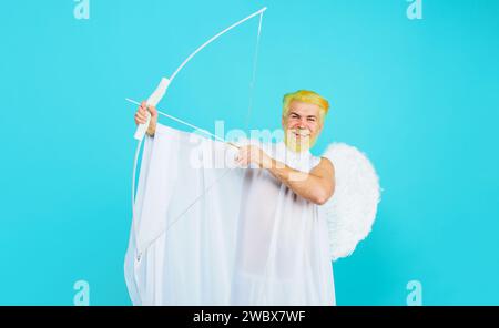 Valentinskuppenengel schießt Pfeile der Liebe. Lächelnder bärtiger Mann im Engelskostüm mit Bogen und Pfeil. Gott der Liebe. Männlicher Cupid in Engelsflügelsprossen Stockfoto