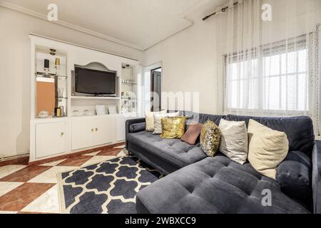 Möbliertes Wohnzimmer eines Hauses mit blauem Samtsofa mit vielen Kissen, eingebautem Bücherregal mit Holztüren Stockfoto