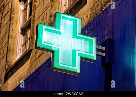 Warminster, Wiltshire, Vereinigtes Königreich - 29. Dezember 2022: Ein beleuchtetes grünes erste-Hilfe-Kreuz an der Fassade von Boots the Chemist in The Warminster, England Stockfoto