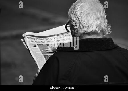 Ross on Wye, Herefordshire, England, 24. September 2023: Mann mit grauem Haar und Brille saß auf einer öffentlichen Bank und las eine Zeitung. Schwarzweißfoto Stockfoto