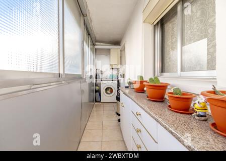 Eine schmale geschlossene Terrasse mit einigen Küchenmöbeln mit einigen Kakteen oben und einer Waschmaschine im Hintergrund Stockfoto