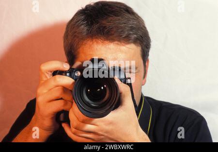 Fotograf mit Kamera, die ein Bild macht, Porträt, Kamera vor dem Gesicht, durch die Kamera schaut Stockfoto
