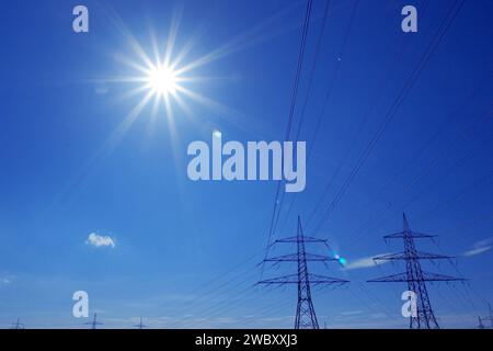 Hochspannungsleitung mit zwei Pylonen gegen blauen Himmel und Sonne Stockfoto