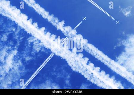 Zwei Flugzeuge mit Kondensstreifen hoch im blauen Himmel, die andere Kondensstreifen überqueren Stockfoto