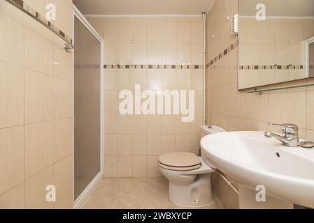 Badezimmer mit rahmenlosem Spiegel an der Wand, Toiletten aus weißem Porzellan, Duschkabine mit synthetischer Glastür mit weißen Aluminiumkanten und verchromtem Meta Stockfoto