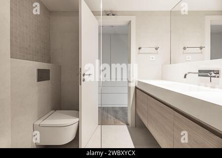 Ein kleines Badezimmer mit Fliesenwänden in Sonnenmarmor-Optik, integriertem Wandspiegel und einteiligem Waschbecken mit Chromhahn. Stockfoto