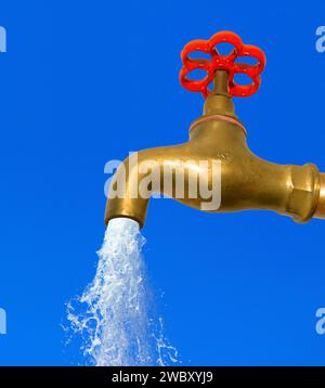 Nahaufnahme eines goldenen Wasserhahns aus Messing mit rotem Griff, Wasser läuft aus ihm Stockfoto