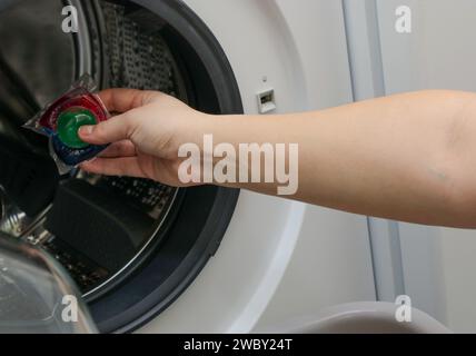 Nahaufnahme einer Frauenhand, die eine Waschgel-Kapsel in eine Waschmaschine legt Stockfoto