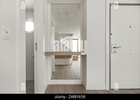 Lobby eines Hauses mit glatten weiß gestrichenen Wänden, einem Ganzkörperspiegel neben der Eingangstür, weißen Einbauschränken, Treppe, passendem Holz Stockfoto