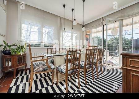 Ein Esstisch mit Glasplatte, Marmorfüßen und Holzstühlen in einem Raum mit Galerien im französischen Stil mit Zugang zur Terrasse. Stockfoto