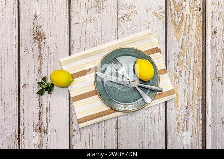 Stillleben mit Porzellanplatten mit Metallbesteck und einigen gelben Zitronen Stockfoto