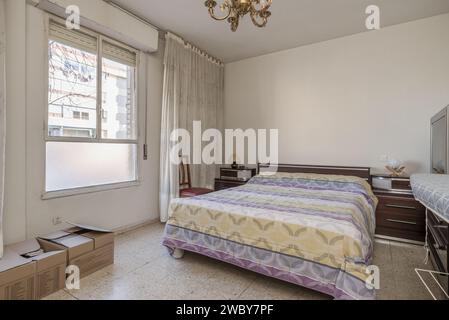 Ein Schlafzimmer aus den 70er Jahren mit einem Doppelbett, Vorhängen an den Fenstern, bedruckter Tagesdecke und Terrazzo-Böden Stockfoto